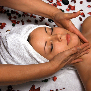 Kosmetik, Kosmetikanwendungen, Eine Frau erhält eine Gesichtsmassage mit Rosenblättern und Steinen um sie herum.